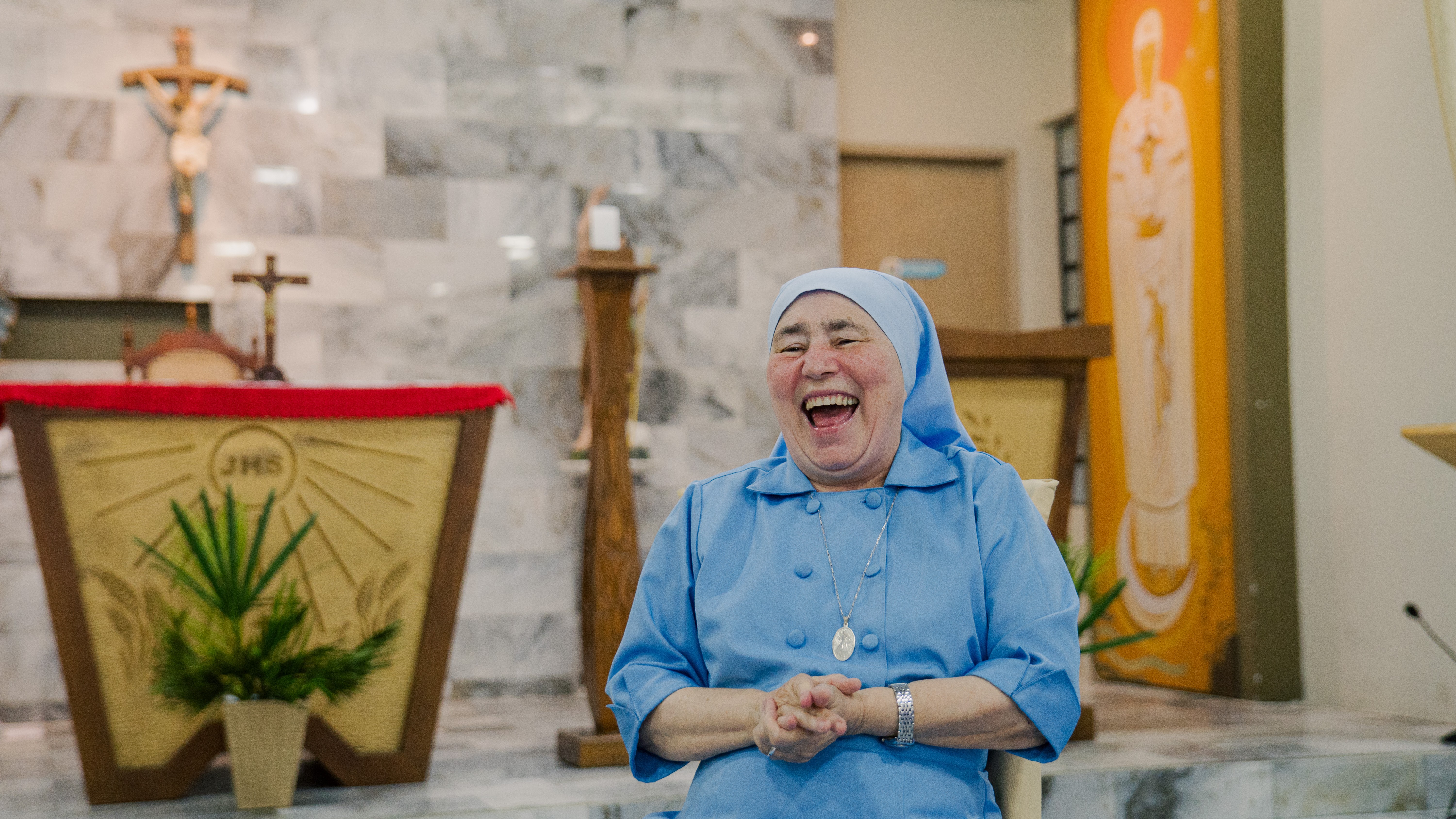 Irmã Conceição sentada numa cadeira na frente de um altar